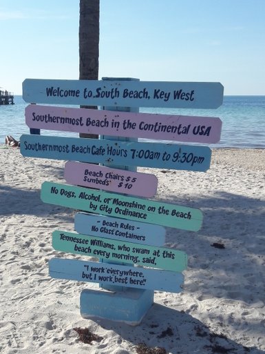 Ein farbenfrohes Schild begrüßt Besucher am South Beach in Key West, umgeben von feinem Sand und Palmen.