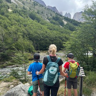Eine Frau steht mit zwei Kindern am Wanderweg und blickt auf die beeindruckenden Berge im Hintergrund.
