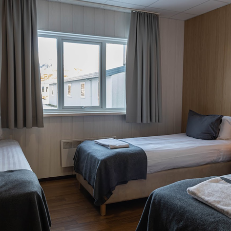 Ein gemütliches Hotelzimmer mit zwei Einzelbetten, einem Fenster mit Blick auf die Berge und einem warmen Licht von einer Lampe.
