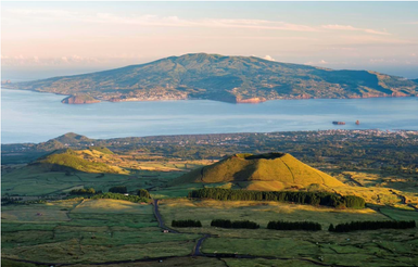 Eine atemberaubende Aussicht auf die grüne Landschaft und den Ozean, mit sanften Hügeln und einem majestätischen Berg im Hintergrund.