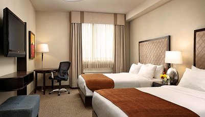 Ein modernes Hotelzimmer mit zwei Betten, einem Schreibtisch und einem Fernseher, das hell und einladend wirkt.