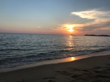 Ein malerischer Sonnenuntergang am Strand, mit sanften Wellen, die das Licht reflektieren und den Himmel in warmen Farben färben.