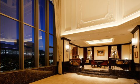 Der Empfangsbereich eines eleganten Hotels mit großen Fenstern, die den Abendhimmel reflektieren und warmes Licht spenden.