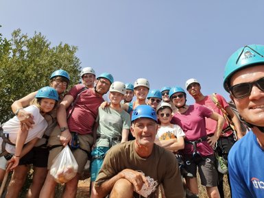 Eine Gruppe von Kletterern in blauen Helmen posiert fröhlich vor einer grünen Kulisse unter blauem Himmel.