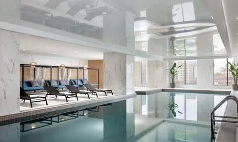 Ein eleganter Innenpoolbereich mit modernen Liegen und großen Fenstern, die viel Tageslicht hereinlassen.