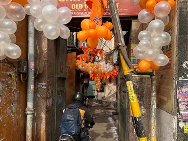 Ein Motorradfahrer fährt durch eine enge Gasse, geschmückt mit orangefarbenen und transparenten Luftballons.