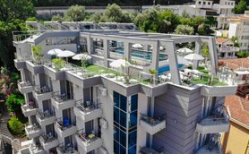 Das moderne Hotel in Budva hat eine Dachterrasse mit Pool und Sonnenschirmen, umgeben von üppigem Grün und bunten Blumen.