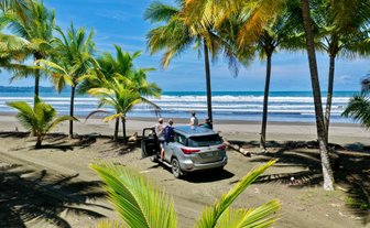 Am Strand von Playa Quepos stehen vier Personen, die das Ocean-View bewundern, während ein Auto im Sand parkt.