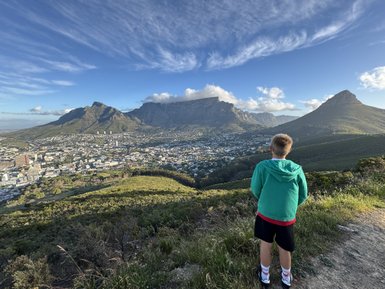 Ein Junge steht auf einem Hügel und blickt auf die Stadt und die majestätischen Berge im Hintergrund.