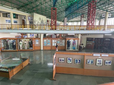 Ein weitläufiger Ausstellungsraum mit Vitrinen, die traditionelle Kleidung und historische Fotos aus Nepal zeigen.