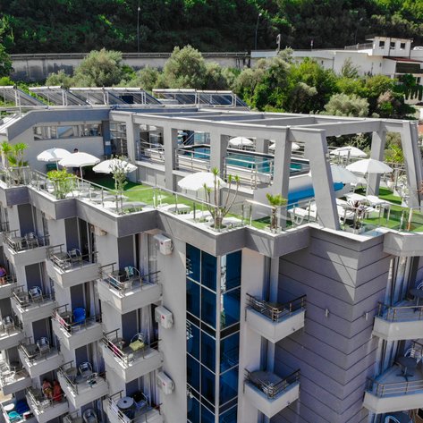 Das moderne Hotel in Budva hat eine Dachterrasse mit Pool und Sonnenschirmen, umgeben von üppigem Grün und bunten Blumen.