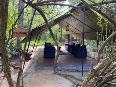 Ein einladender Entspannungsbereich unter einem Zelt, umgeben von üppigem Grün und einem Holzschild mit der Aufschrift 'RELAXING AREA'.