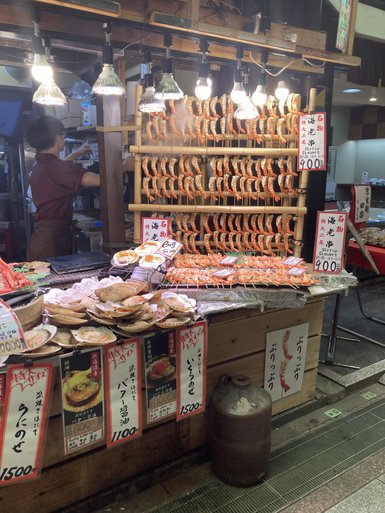 Ein Marktstand in Kyoto bietet eine Vielzahl von gegrillten Garnelen und Meeresfrüchten, umgeben von warmem Licht.