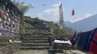 Eine steinerne Treppe führt zu einem Aussichtspunkt, umgeben von bunten Gebetsfahnen und einem klaren blauen Himmel.