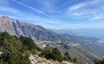 Ein atemberaubender Blick auf die Berge und das Meer, umgeben von üppigem Grün und klarem, blauem Himmel.