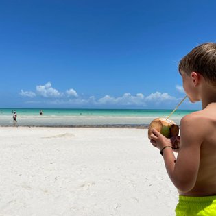 Kind trinkt frisches Kokosnusswasser am Strand von Puerto Morelos – Mexiko Familienreise