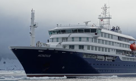 Das Schiff 'Hondius' liegt majestätisch im Wasser, umgeben von Eis und einer dramatischen, bewölkten Landschaft.