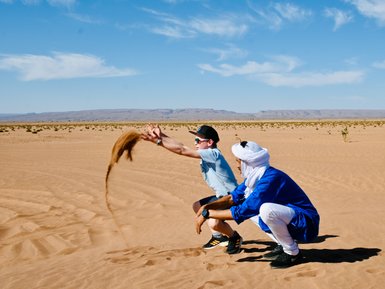 Guide und Kind spielen gemeinsam und werfen Sand in der weiten Wüste – Familienreise nach Marokko