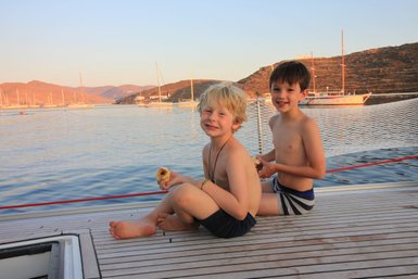 Zwei fröhliche Jungen sitzen auf dem Deck eines Bootes und genießen frisches Obst, während die Sonne untergeht.