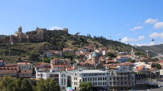 Eine malerische Aussicht auf Tiflis mit bunten Häusern und einer beeindruckenden Festung auf dem Hügel im Hintergrund.