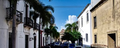 Eine malerische Straße in Santo Domingo, gesäumt von historischen Gebäuden und üppigen Palmen unter einem strahlend blauen Himmel.