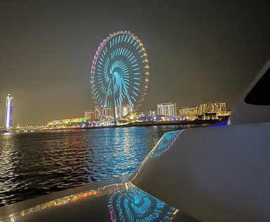 Ein beleuchtetes Riesenrad spiegelt sich im Wasser, während eine Yacht im Vordergrund sanft schaukelt.