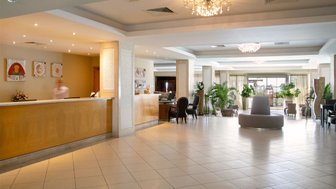 Der Empfangsbereich des Atlantica Miramare Beach Hotels mit eleganter Einrichtung und einem freundlichen Mitarbeiter im Hintergrund.
