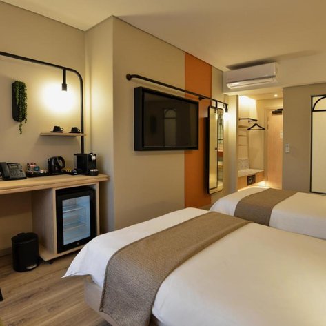Ein modernes Hotelzimmer mit zwei Einzelbetten, einem Schreibtisch und einem Fernseher an der Wand.