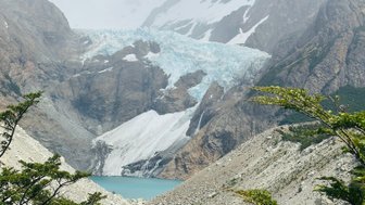 Ein majestätischer Gletscher erstreckt sich über die Berge, umgeben von grünen Bäumen und einem klaren blauen See.