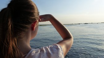 Eine Person mit langen Haaren schaut nachdenklich über den Chobe-Fluss, während die Sonne am Horizont untergeht.