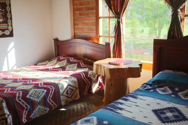 Ein gemütliches Zimmer mit zwei Betten, die mit bunten Decken bedeckt sind, und einem rustikalen Holztisch in der Mitte.