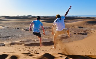 Kinder springen und haben Spaß auf den weiten Sanddünen der Sahara – Marokko Familienreise