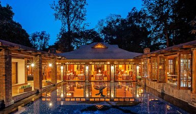 Ein elegantes Lodge-Gebäude mit großen Fenstern spiegelt sich im ruhigen Pool bei Dämmerungslicht wider.
