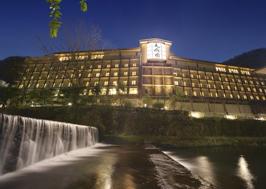 Ein elegantes Onsen-Hotel in Hakone, beleuchtet bei Nacht, mit einem sanften Wasserfall im Vordergrund.