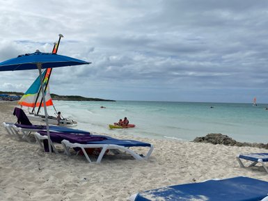 Am Strand von Cayo Santa Maria sind Liegen auf dem Sand platziert, während Segelboote und Kajaks im Wasser aktiv sind.