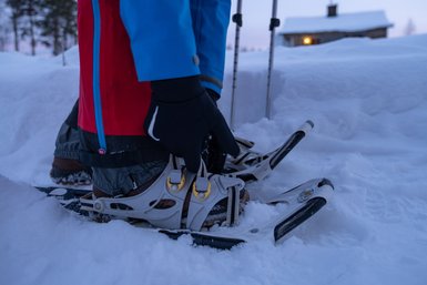 Ein Fuß in Schneeschuhen steht im frischen Schnee, während die Umgebung in sanftem Licht erleuchtet ist.