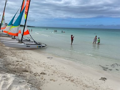 Am Strand von Cayo Santa Maria stehen Segelboote mit bunten Segeln, während Familien im flachen Wasser spielen.
