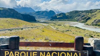 Ein Holzschild mit der Aufschrift 'Parque Nacional Los Glaciares' steht vor einer beeindruckenden Berglandschaft.