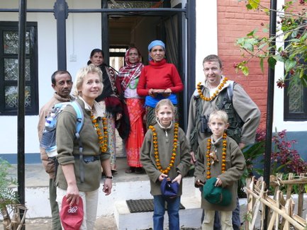 Eine Familie steht vor einem Haus in Nepal, umgeben von Einheimischen, die traditionelle Kleidung tragen und freundlich lächeln.