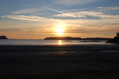 Ein atemberaubender Sonnenuntergang über dem ruhigen Wasser, das sanft den Strand von Tofino umspielt.