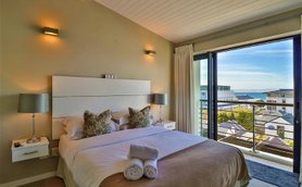 Ein elegantes Hotelzimmer mit einem großen Bett, dekorativen Kissen und Blick auf das Meer durch große Fenster.