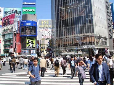 Eine belebte Straßenkreuzung in Shibuya, Tokyo, mit vielen Fußgängern, die über die Zebrastreifen gehen.