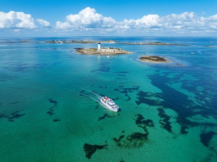 Ein Boot fährt durch das klare, türkisfarbene Wasser, umgeben von kleinen Inseln und einem strahlend blauen Himmel.