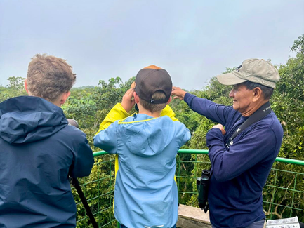 Drei Personen stehen auf einer Aussichtsplattform im Dschungel und beobachten die Umgebung mit Ferngläsern.