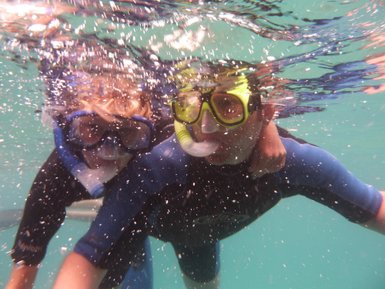 Zwei Kinder in Taucheranzügen genießen das Schnorcheln unter Wasser, umgeben von sprudelnden Blasen und klarem Wasser.