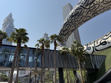 Eine moderne Architektur mit einem geschwungenen, kunstvoll gestalteten Überbau und Palmen im Vordergrund in Dubai.