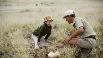 Ein Guide zeigt einem Kind ein großes Straußenei - Namibia mit Kindern