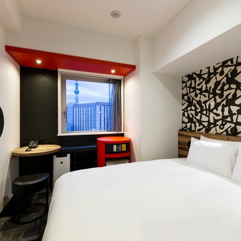 Ein modernes Hotelzimmer mit einem großen Bett, einem kleinen Tisch und einem Fenster, das den Tokyo Skytree zeigt.