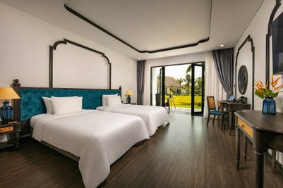 Ein elegantes Zimmer mit zwei Einzelbetten, blauen Akzenten und Blick auf einen grünen Garten durch große Fenster.