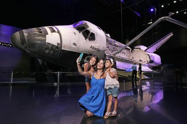 Drei Frauen posieren fröhlich für ein Selfie vor dem Space Shuttle Atlantis im Kennedy Space Center.
